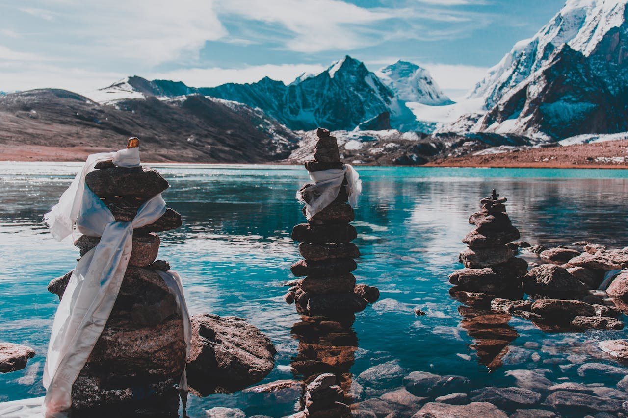 ours-journey Calm lake scene with majestic snow-capped mountains and tranquil rock cairns.