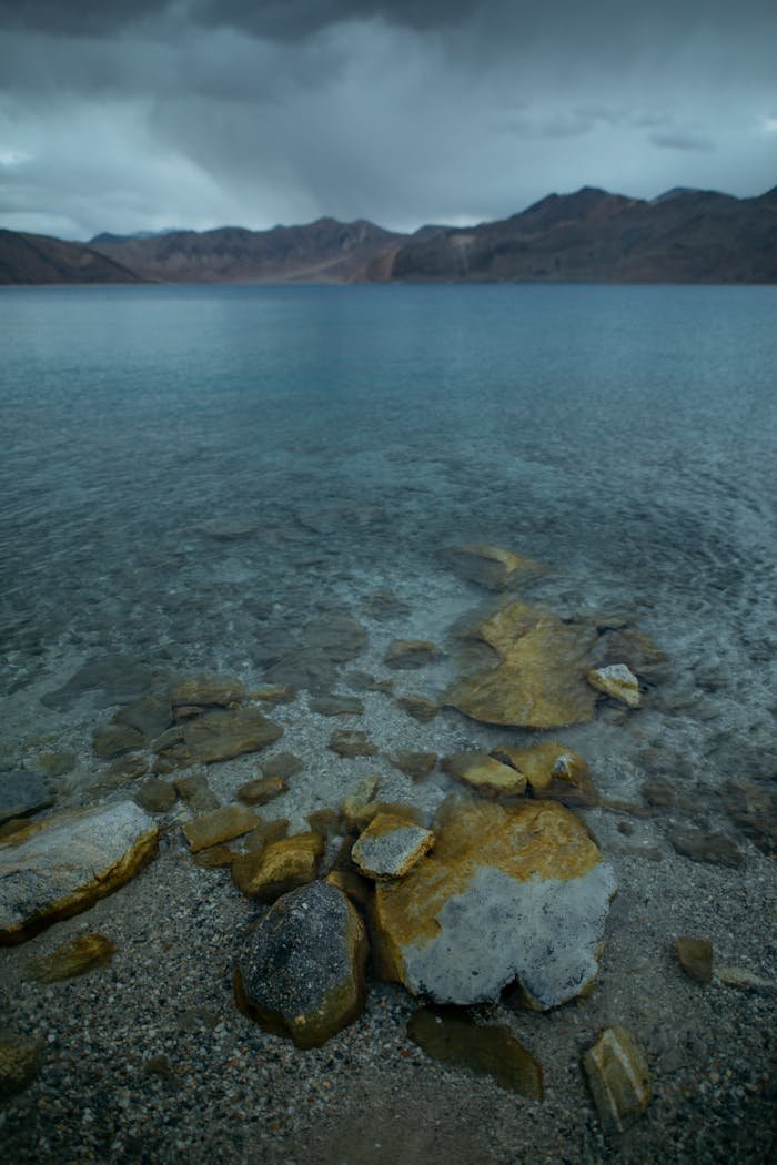 services-03 Pangong Lake with clear water and distant mountains under a cloudy sky.